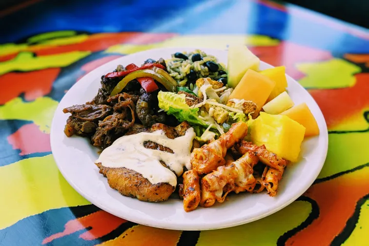 Colorful plate with meat, rice, pasta, fruits, and veggies.