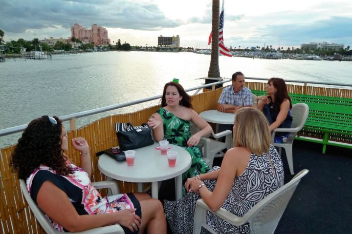 Group of people sitting at tables on a boat overlooking water.