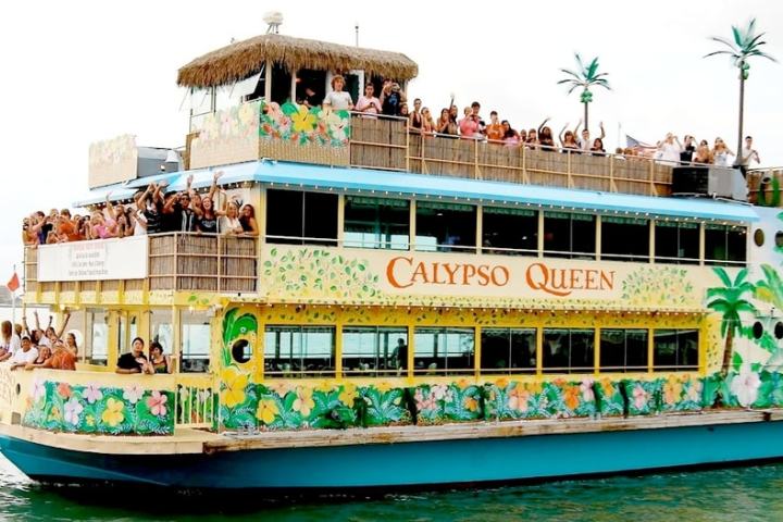 Colorful cruise boat 'Calypso Queen' on water, decorated with palm trees, full of people.
