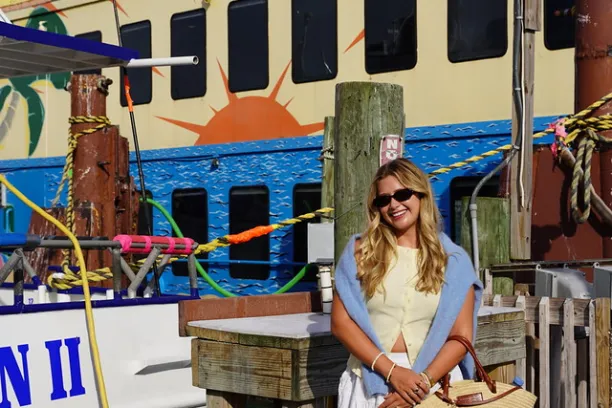 Woman in white dress, sunglasses, stands near boat with 'Calypso Breeze' sign.