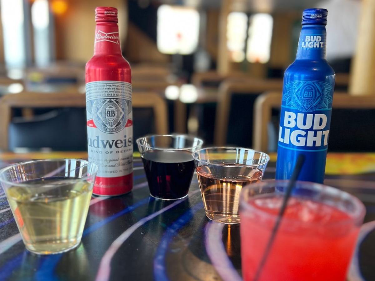 Table with assorted drinks including Budweiser, Bud Light, and various beverages in plastic cups.