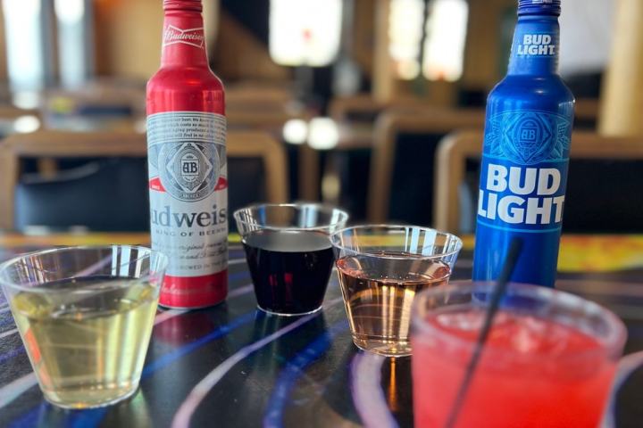 Table with assorted drinks including Budweiser, Bud Light, and various beverages in plastic cups.