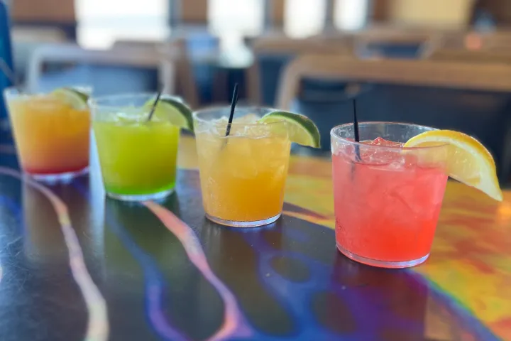 Four colorful cocktails with lime slices on a patterned table.