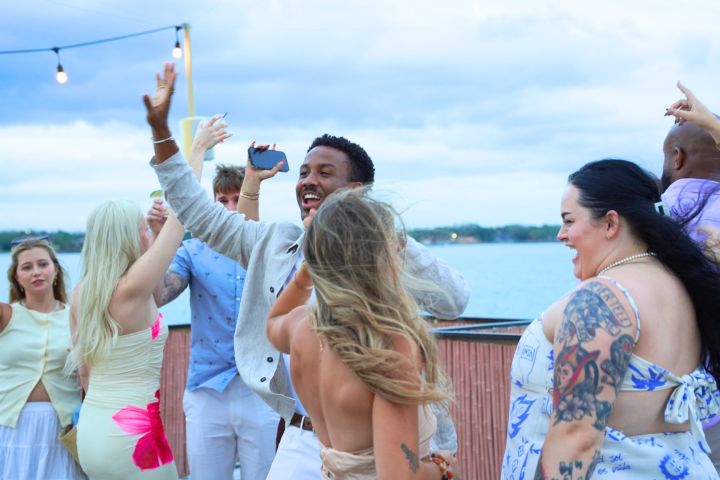 Group of people dancing joyfully at an outdoor event near a body of water.
