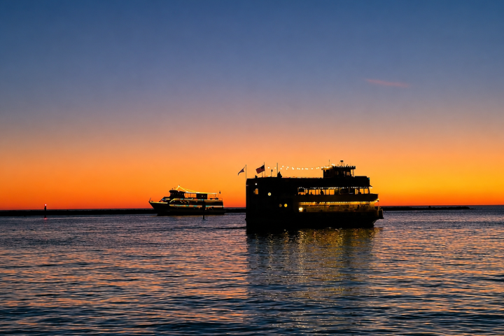 Two boats on the water at sunset with an orange sky.