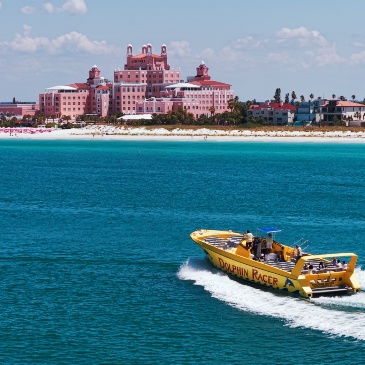 Boat named 'Dolphin Racer' on blue water with a pink hotel and beach in background.