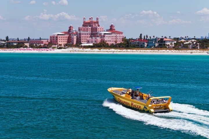 Boat named 'Dolphin Racer' on blue water with a pink hotel and beach in background.