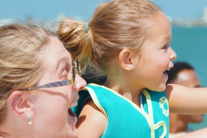 Woman and child smiling by the ocean on a sunny day.