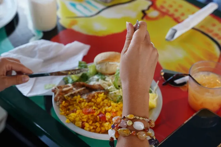 Person dining with colorful plate, phone, and drinks on table.
