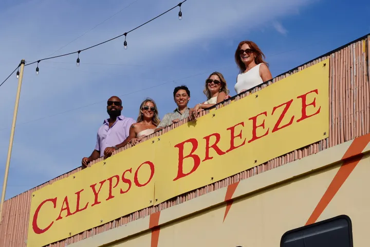 Five people stand on 'Calypso Breeze' boat under string lights.