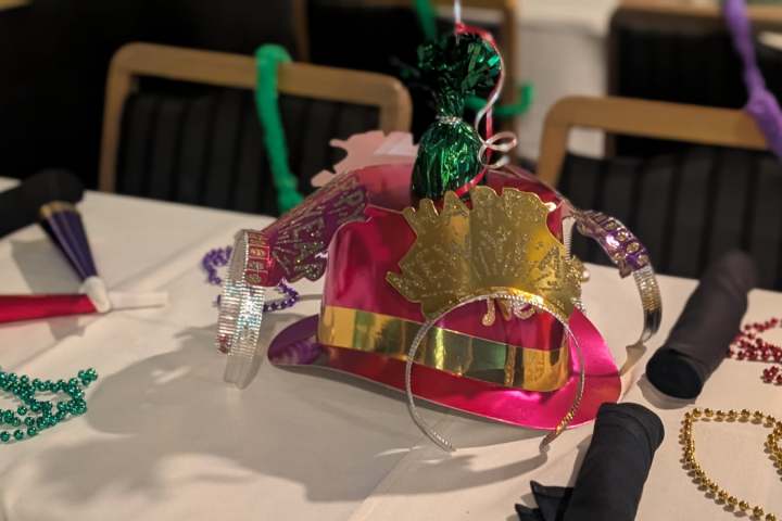 Festive hat with decorations on a table with colorful beads and streamers.