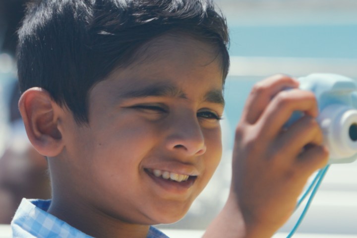 Smiling boy holding a light blue camera outdoors.