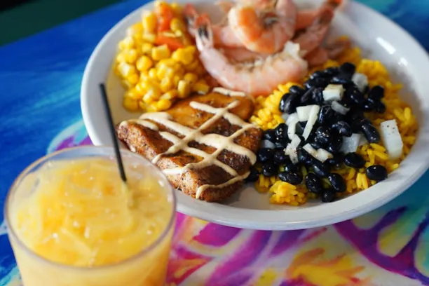 Plate with shrimp, corn, black beans, toast; juice in glass, colorful table.