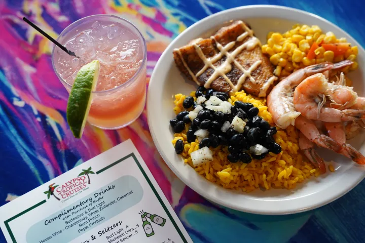 Plate with shrimp, corn, fish, rice, and beans next to a pink drink and menu.