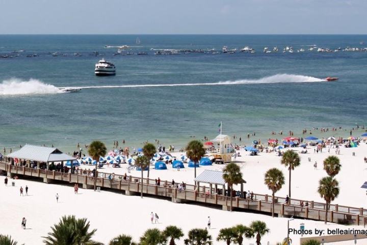 Beach scene with people, boats in water, and pier with palm trees.