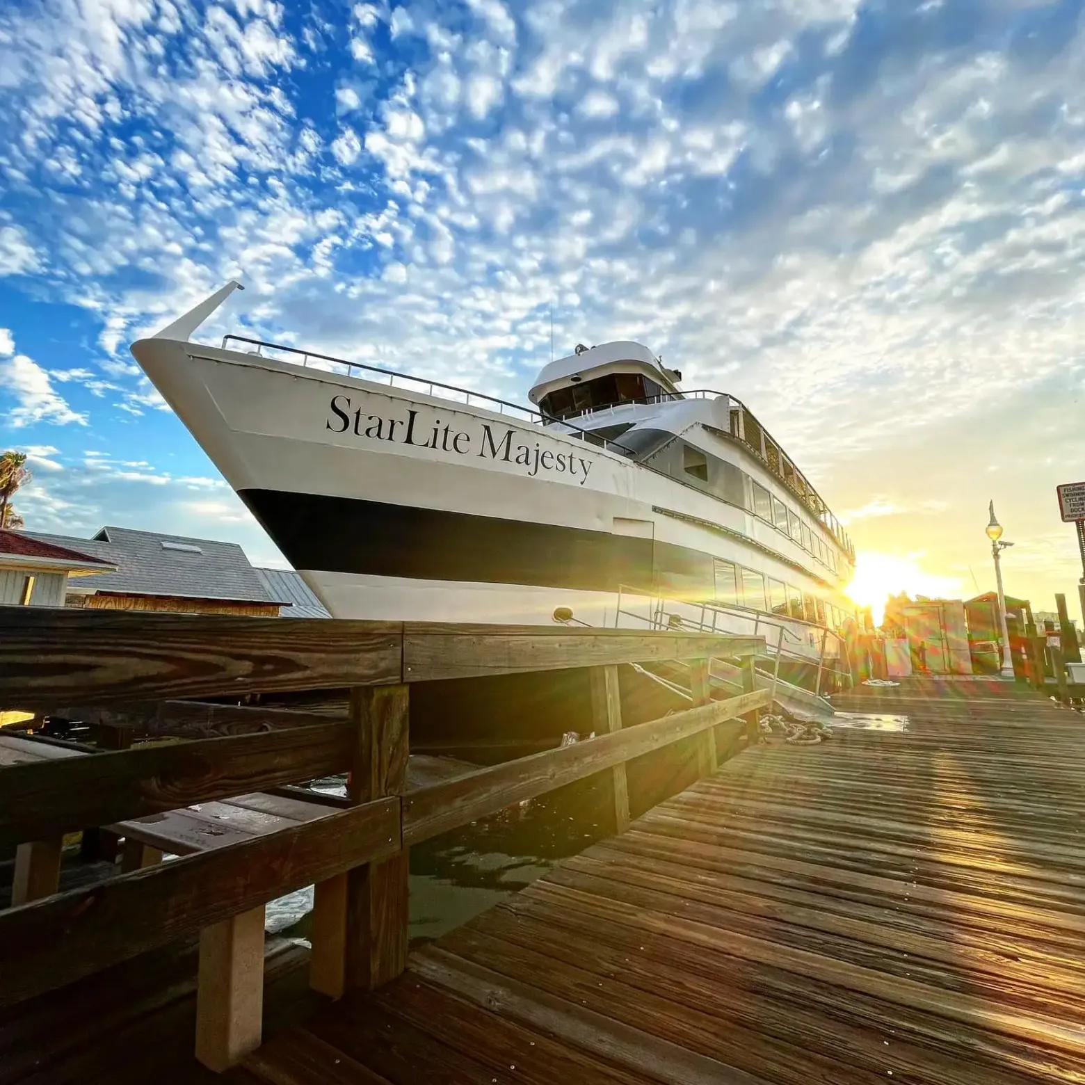 Large boat named 'StarLite Majesty' docked at sunrise with wooden pier and cloudy sky.