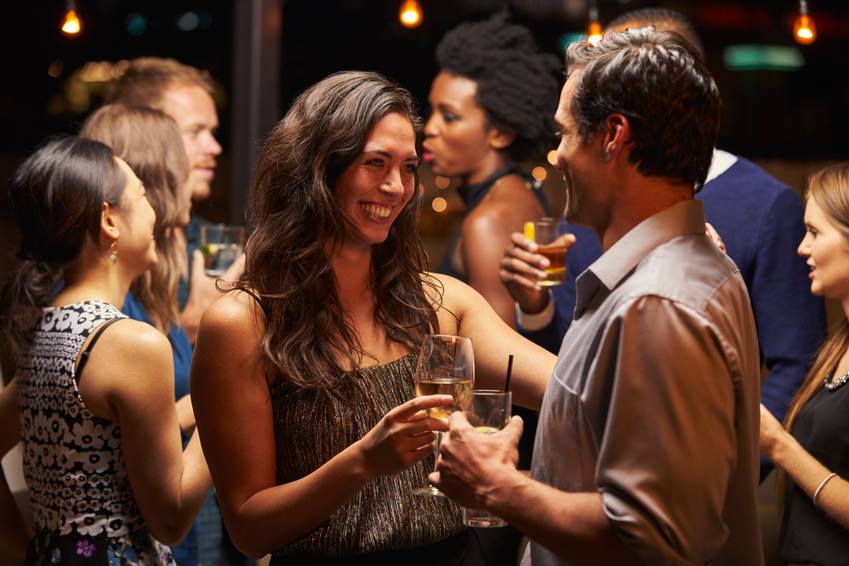 People socializing at a party, holding drinks and smiling in a lively atmosphere.