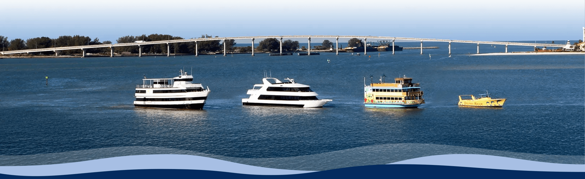 Four boats on a calm sea with a bridge in the background and clear blue sky.