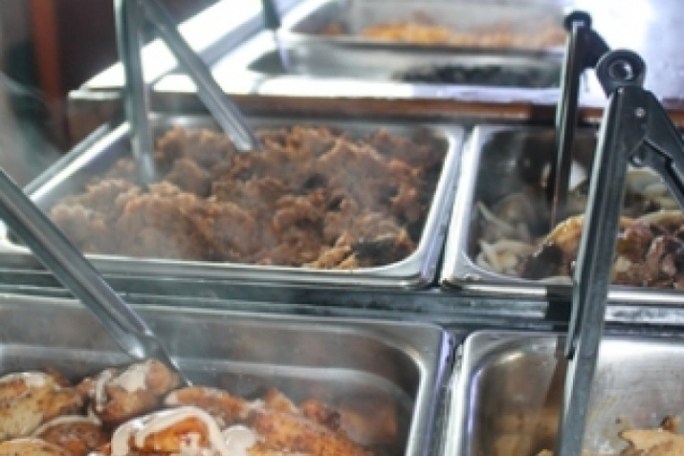 Buffet with steaming trays of cooked meat and serving tongs.