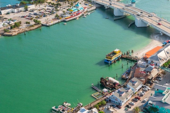 Aerial view of a coastal town with a bridge over turquoise water and colorful buildings.