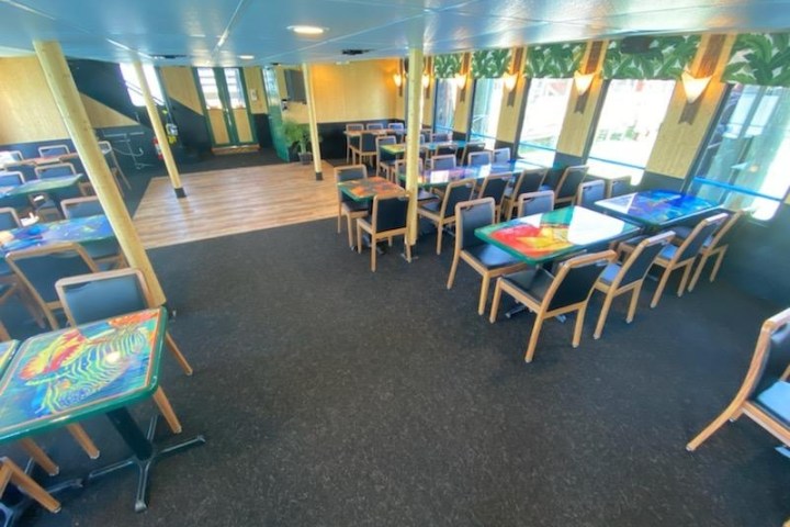 Bright dining area with colorful tables and chairs, windows on the right, and decorative ceiling lights.