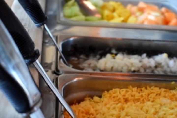 Food buffet with utensils, featuring fruits and grated cheese in metal trays.