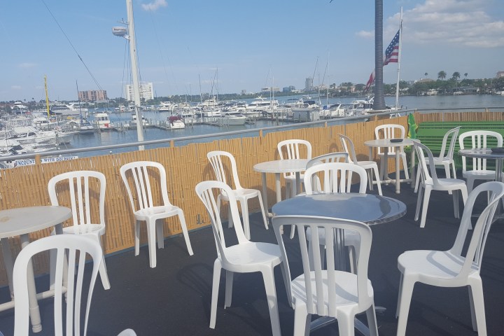 Outdoor patio with white chairs, tables, and a marina view with boats and American flag.