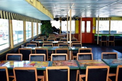 Empty dining area on a boat with tables, chairs, and large windows.