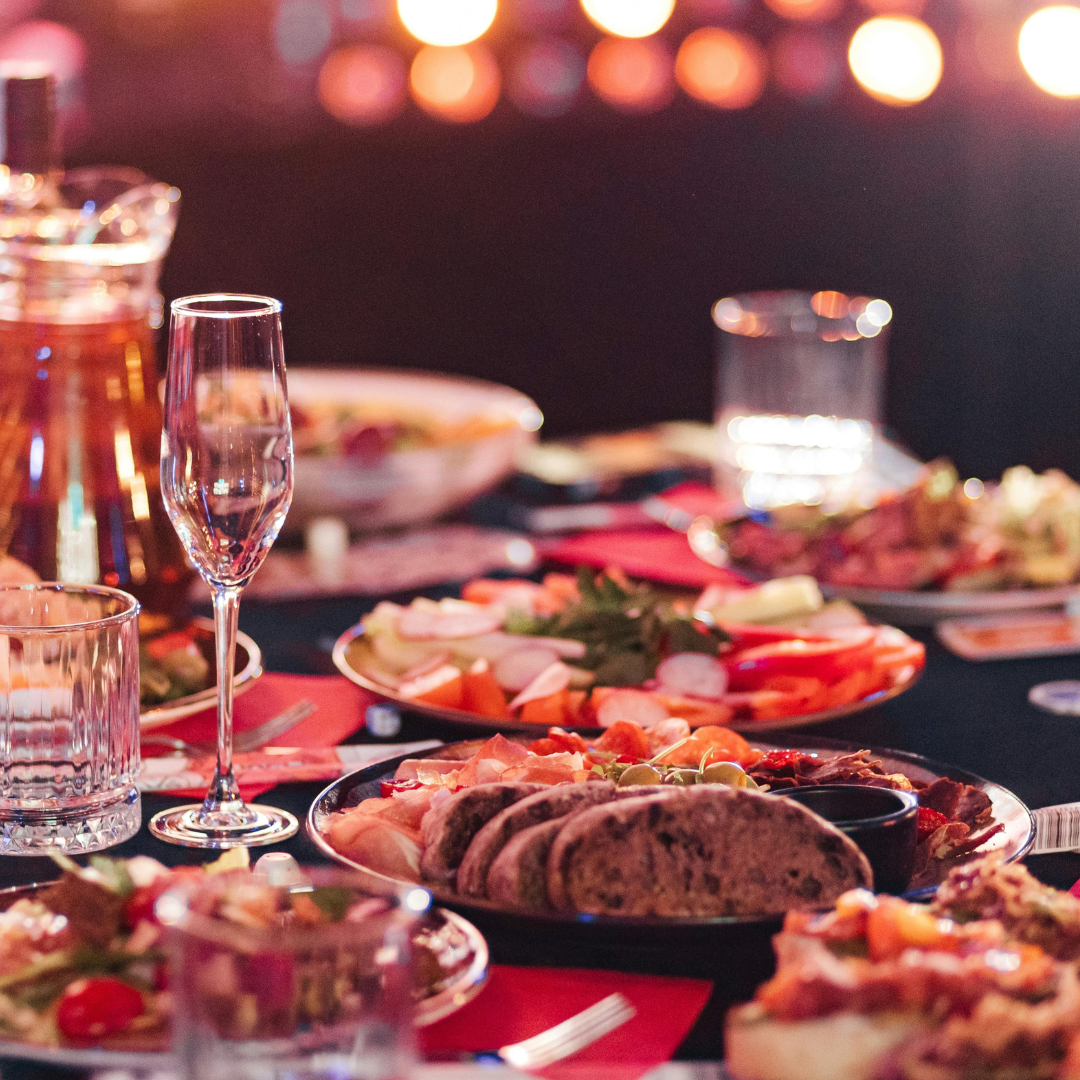 A table set with drinks, glasses, and a variety of plated foods in a dimly lit setting.