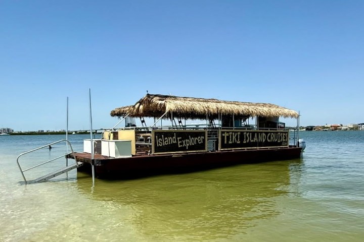 A tiki-style boat named 'Island Explorer' on calm water under a blue sky.