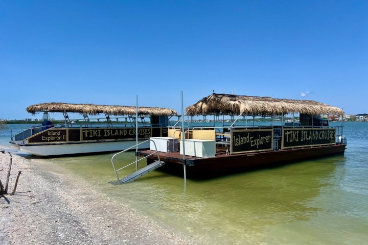 Two tiki-style boats docked on a sandy shoreline under a clear blue sky.