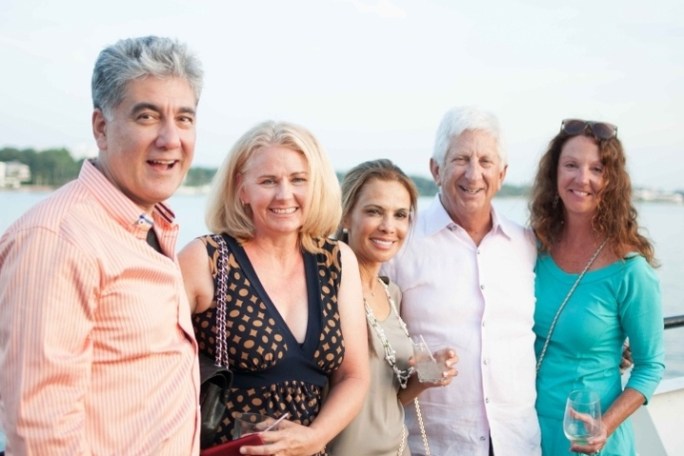 Five people smiling, posing outdoors near water, holding drinks.