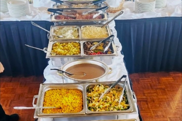 Buffet table with various chafing dishes of food, including vegetables, meat, and sauces.