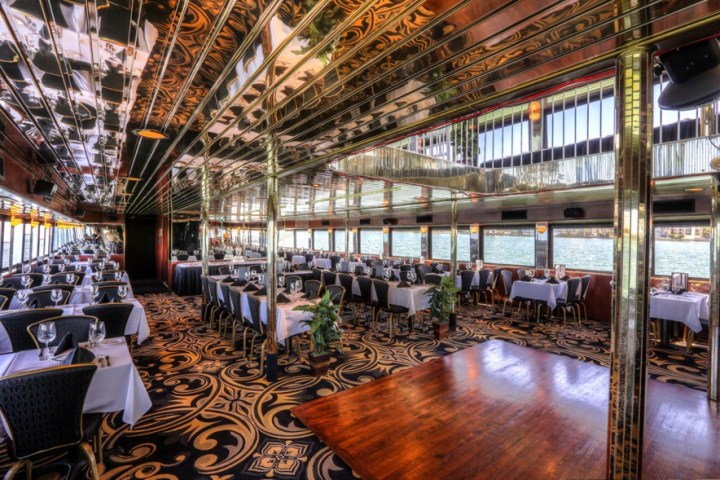 Elegant dining area on a boat with ornate carpet, mirrored ceiling, and large windows overlooking water.