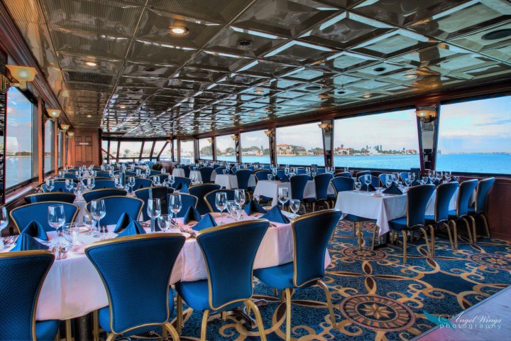 Elegantly set dining area on a boat with blue chairs and sea view through large windows.