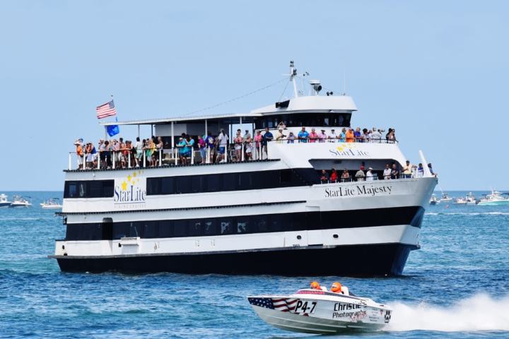 Large cruise boat named StarLite Majesty with people, passing by a speedboat on the ocean.