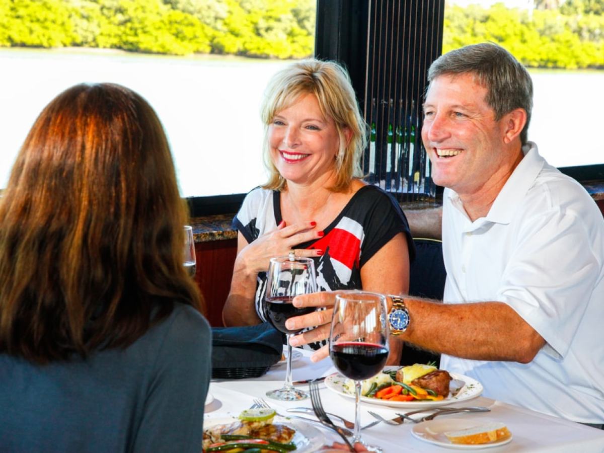 Three people enjoying a meal with wine by a window with a view of greenery outside.