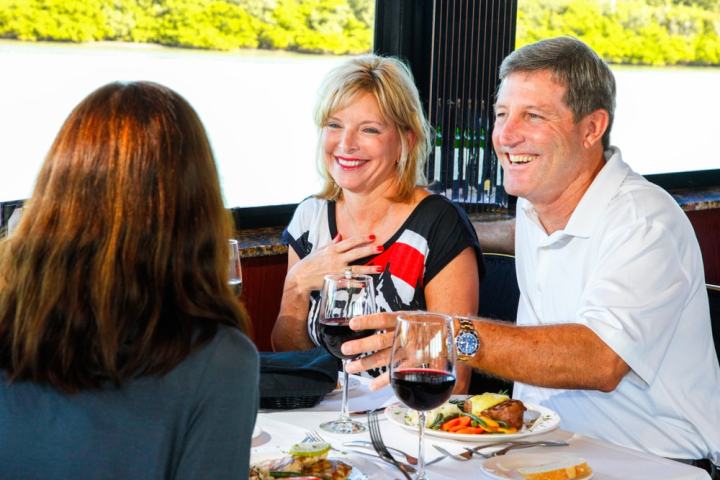 Three people enjoying a meal with wine by a window with a view of greenery outside.