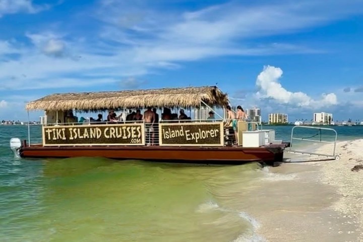 Tiki Island Cruises boat docked on sandy shore under a clear blue sky.