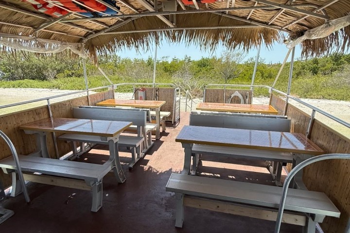 Open-air boat with bench seating and thatched roof, life vests above.