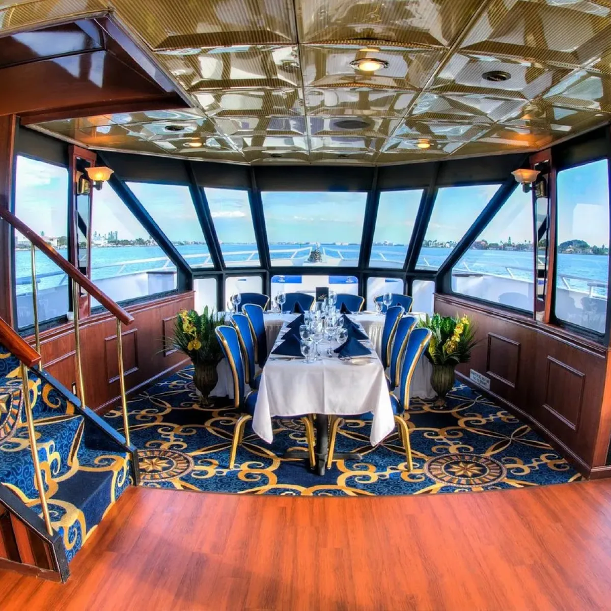 Luxurious yacht interior with dining table, elegant carpet, and panoramic windows overlooking water.