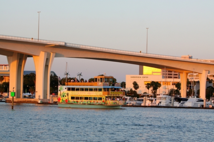 Colorful boat on water near bridge, set against a sunny cityscape.