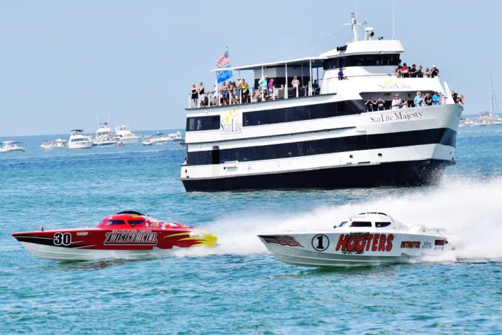 Two speedboats racing near a large passenger boat on a sunny day.