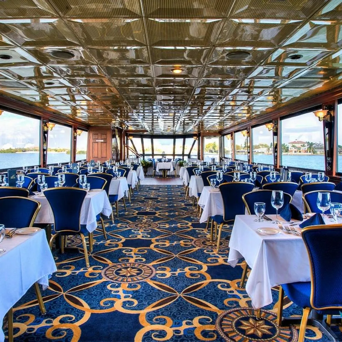 Elegant boat dining room with blue chairs, white tablecloths, and large windows overlooking water.
