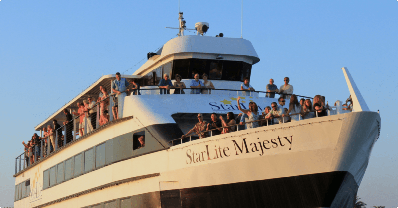 Large white boat, 'StarLite Majesty,' with many people on deck enjoying a sunny day.