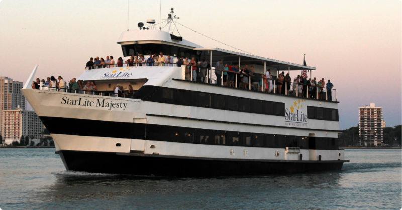 Large white cruise boat on the water with people on deck during sunset.
