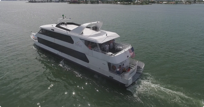A white yacht cruising on a calm body of water with passengers on the deck.