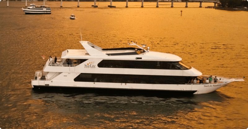 White cruise boat on a golden waterway at sunset, with a bridge in the background.