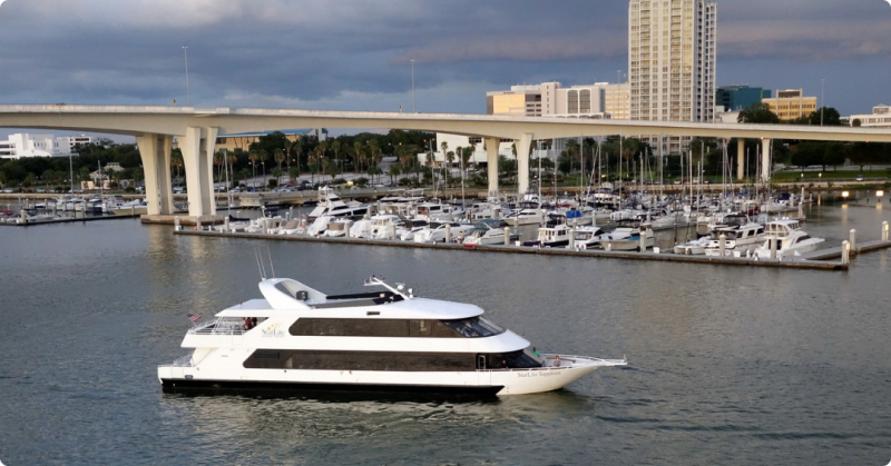 White yacht on water near a marina, with a bridge and city skyline in the background.