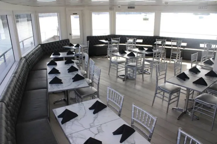 Elegant dining room with marble style tables and silver chairs, black napkins on each table.